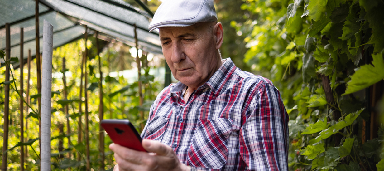 Un homme âgé à l'extérieur regardant son téléphone avec inquiétude.