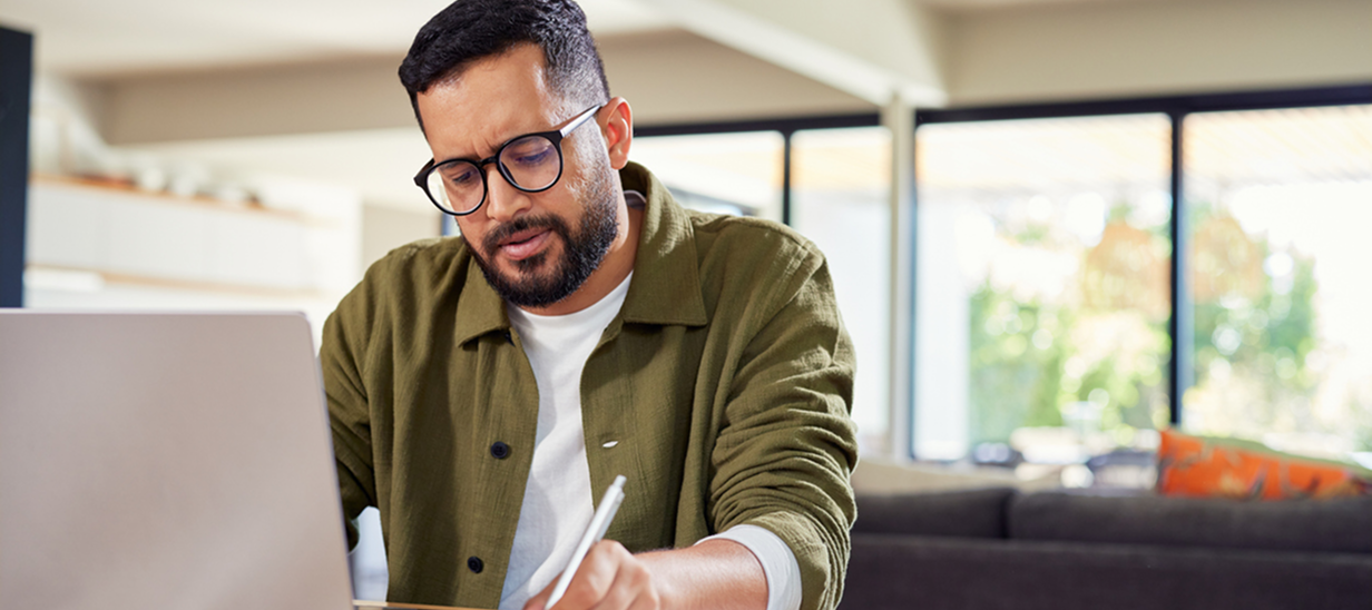 un jeune homme regardant son ordinateur avec inquiétude et écrivant sur un bloc-notes